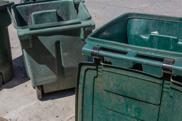 Large green trash cans, empty with lids open, curbside, horizontal aspect