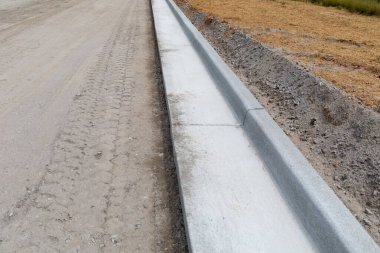 Yeni yol yapım aşamasında, toprak yolun yanında beton kaldırım, kamış ve erozyon koruması, yatay görünüm