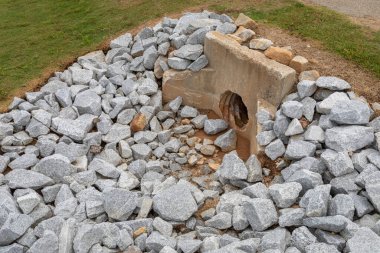 Yeni granit kaya sulama ve erozyon kontrolü ile çevrili eski döküm beton başlık, yeşil çimen, menfez aşınma gelişimi, yatay görünüm