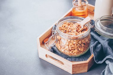Sağlıklı kahvaltı için-malzemeler granola, süt veya yoğurt ve bal. Granola cam ahşap tepsi. Metin için yer kopyalayın.