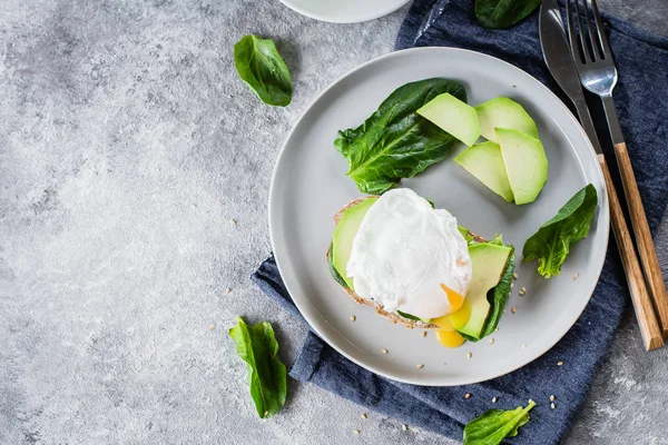 Sandwich with avocado, spinach and poached egg on whole wheat bread on plate on stone background