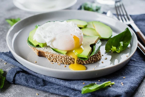Sandwich with avocado, spinach and poached egg on whole wheat bread on plate on stone background