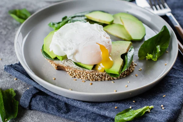 Sandwich with avocado, spinach and poached egg on whole wheat bread on plate on stone background