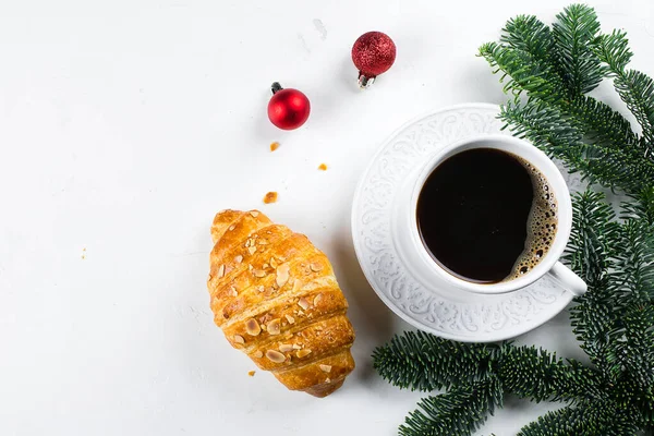 Winter breakfast flat lay. Taza de café negro, croissant y decoración navideña, ramas de abeto sobre fondo de mesa blanco. Vista superior, espacio de copia — Foto de Stock