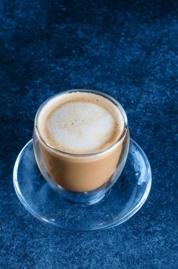 Mavi lacivert arka plan masasında cam bardakta bir fincan kahve. Uzayı kopyala Sabah içkisi kapuçino.