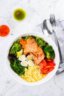 Sağlıklı yemek, keto yemek konsepti. Balık salatası kasesi mermer masa arkasında. Somonlu salata, kuskus, sebze, bıldırcın yumurtası. Üst görünüm, alanı kopyala