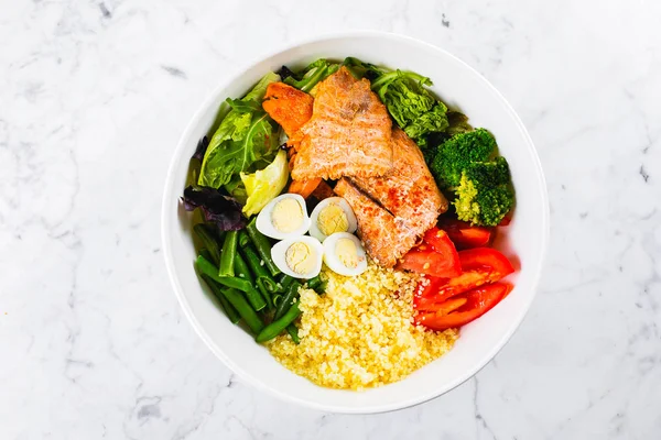 Здоровое питание, концепция кето-питания. Рыбный салат на мраморном фоне. Салат с лососем, кускус, овощи, перепелиные яйца. Вид сверху, пространство для копирования — стоковое фото