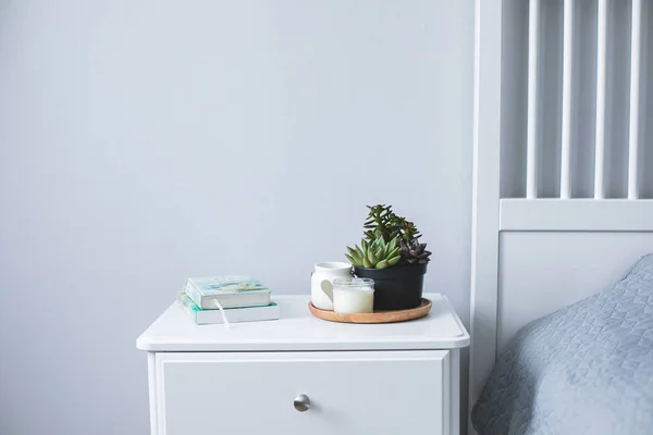 Tiny succulents, candles and books on bedside table in the bedroom in scandinavian style home. Scandinavian interior in gray and white colors