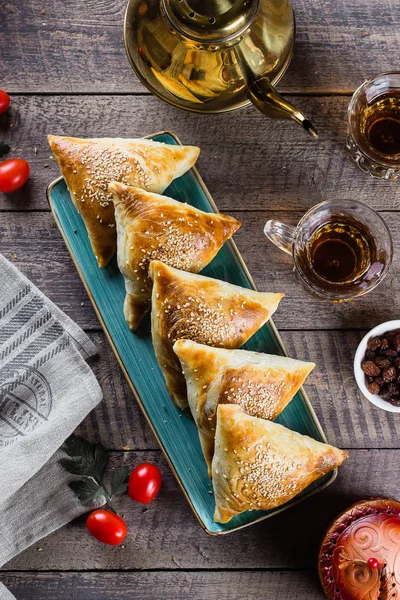 Cozinha oriental. Samosas deliciosas samsa com carne, vidro de chá em fundo de mesa de madeira, vista superior. Comida Ramadã — Fotografia de Stock