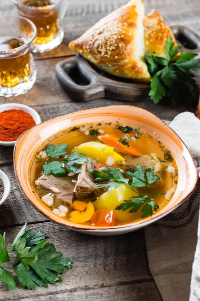Asijská polévka shurpa s masem a zeleninou v talíři na dřevěném stole. — Stock fotografie