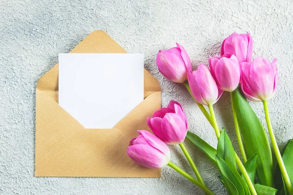 Mother's day Holiday Concept. Pink tulips flowers and empty card on concrete background. Greeting card for Womens or Mothers Day. Flat lay, top view, copy space. Mockup concept.