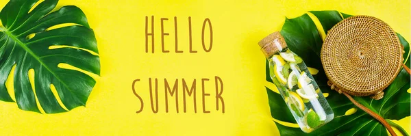 Hallo Zomer Banner voor website. Ronde rotan zak en glazen fles met limonade en Monstera blad. Gele, zonnige achtergrond. Vlakke lay, bovenaanzicht — Stockfoto