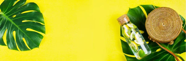 Summer Banner για την ιστοσελίδα. Στρογγυλή τσάντα μπαστούνι και γυάλινο μπουκάλι με λεμονάδα και φύλλα Monstera. Κίτρινο, ηλιόλουστο φόντο. Επίπεδο lay, πάνω όψη — Φωτογραφία Αρχείου