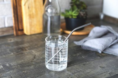 Mutfak masasında metal pipetli bir bardak su. Eko doğal, sürdürülebilir yaşam tarzı, sıfır atık, plastiksiz konsept.