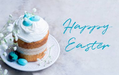 Mutlu Paskalyalar. Geleneksel Paskalya Pastası Kulich süslemeli krema ve mavi şeker kamışlı gri masa arkasındaki tabakta yumurta şekilli..