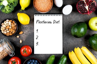 Flexitarian Diyet Konsepti. Yeşil sebzeler, domatesler, fındıklar, meyveler, mercimekler, nohutlar, yeşiller ve gri beton masada boş bir defter. Düz konum, üst görünüm, kopyalama alanı