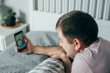 Genç adam annemle görüntülü konuşma yapıyor. Aile, karantinada iletişim kurmak için telefonu kullanıyor. Evde kal, kendini izole et, güvende ol.