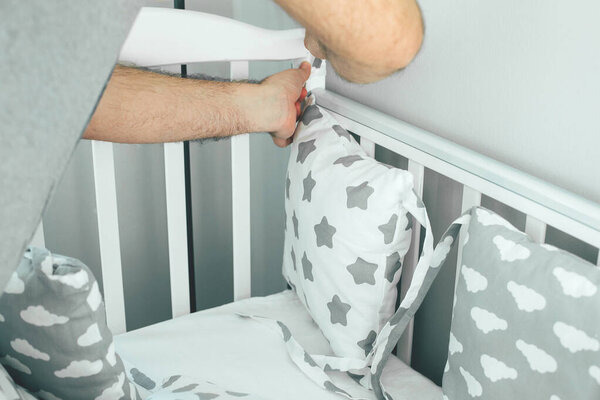 Father helps young mother put on bumpers in the crib. Family lifestyle concept