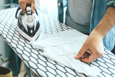 Genç baba bebek kıyafetlerini ütülüyor. Ev işi kavramı, ev işleri, karantina dönemindeki ev işleri. Evde kal..