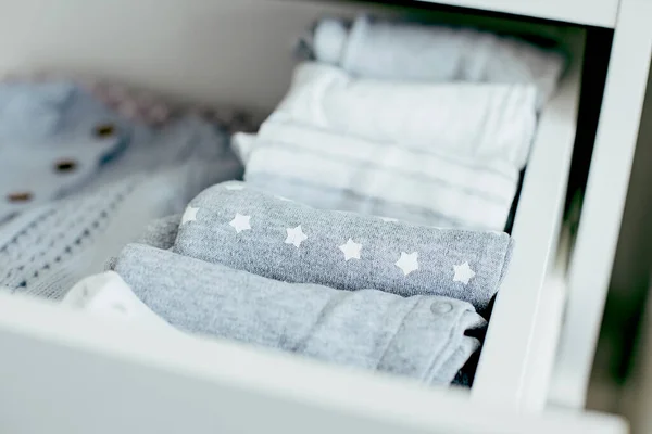 Baby or newborn things of white, blue and grey colors are in the drawer. Lady fly system, kondo, konmary concept. Home lifestyle.