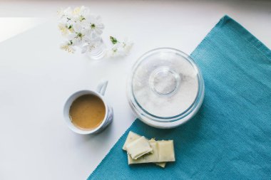 süt, şeker, beyaz çikolata, çiçek ve beyaz bir arka plan mavi bir peçeteye kahve