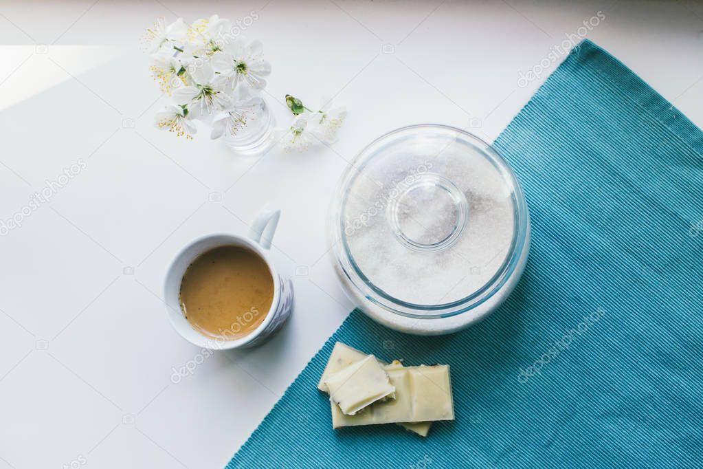 cup of coffee with milk, sugar, white chocolate, flowers and a blue napkin on a white background