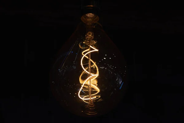 Large decorative incandescent lamp on a dark background. Numerous light sources are reflected in a glass bulb