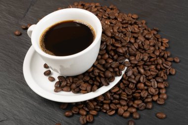 Siyah arka planda kahve fincanı ve kahve çekirdekleri.