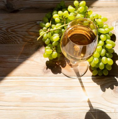 Güneşli bir günde bir sürü üzümlü arka planda beyaz şarap kadehi. Altın üzümlü, köpüklü şarap kadehi ahşap şaraphane masasının üstünde.