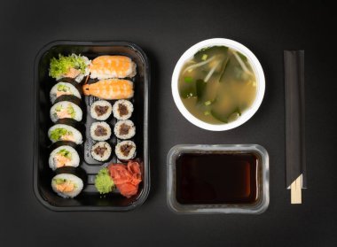 Suşi seti, soya sosu ve miso çorbası hazır. Siyah arkaplan görünümlü susi dürümlü beslenme çantasını kaldır.