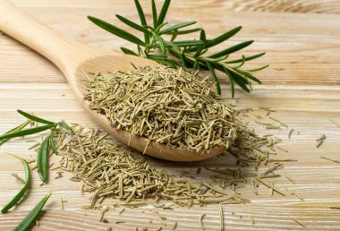 Tahta kaşıkta kuru biberiye iğneleri yığını. Kurutulmuş ezilmiş ve taze yeşil biberiye yaprakları. Baharat, baharat ve otlar kapanıyor.