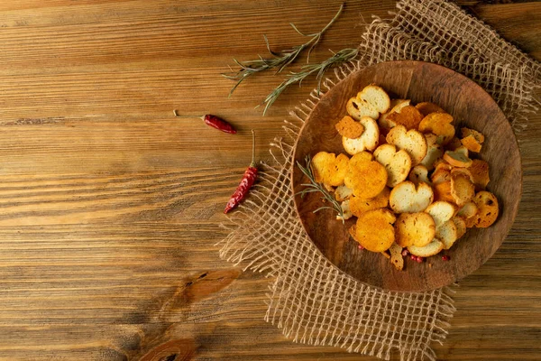 Homemade hot crunchy croutons in rustic style top view with copy space. Round spicy bruschetta crackers, seasoning rusks or small fried bread snacks on wooden plate top view — Stock Image Homemade Hot Crunchy Croutons Rustic Style Top View Copy Space Royalty Free Stock Images