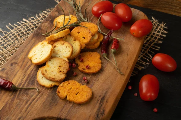 Homemade hot crunchy croutons in rustic style on wooden cutting board. Round spicy bruschetta crackers, seasoning rusks or small fried bread snacks — Stock Image Homemade Hot Crunchy Croutons Rustic Style Wooden Cutting Board Spicy Royalty Free Stock Photos