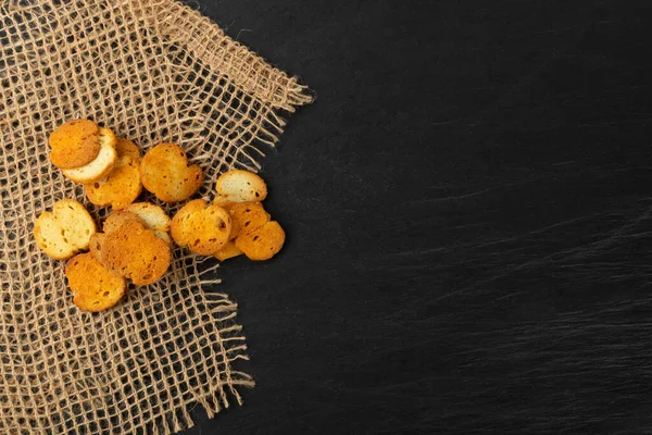 Homemade crunchy croutons in rustic style top view. Round spicy bruschetta crackers, seasoning rusks or small fried bread snacks on black stone slate top view — Stock Image Homemade Crunchy Croutons Rustic Style Top View Spicy Bruschetta Crackers Royalty Free Stock Photos