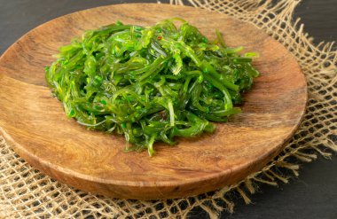 Green Chuka Seaweed Salad on Rustic Background. Wakame Sea Kelp Salat, Chukka Sea Weed, Healthy Algae Food on Wooden Plate clipart