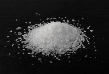 Siyah arka planda büyük şeker kristalleri yığını var. Sukroz kristalleri, deniz tuzu kayaları ya da yiyecek tabakasında granüle edilmiş sodyum tuz dokusu.