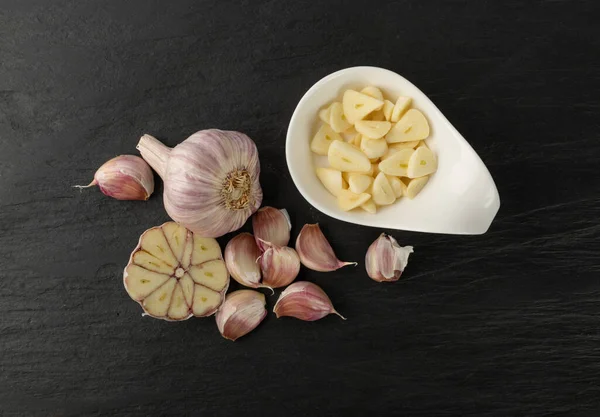 Fresh sliced garlic on black stone background top view. Heap of chopped garlic cloves and garlic head on food slate