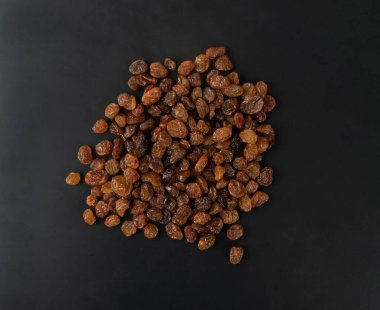 Siyah arka planda bir yığın tatlı kuru üzüm. Kurumuş üzüm yığını, bir avuç koyu kahverengi kuru üzümlü üst görünüm düzlüğü