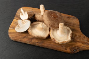 Tahta kesim tahtasında taze şitake mantarı yığını. Çiğ bok, sağlıklı organik Asya mantarı.