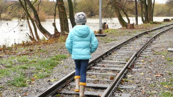 Una chica caminando por las vías del tren. Vista trasera de una chica sobre los rieles . — Vídeos de Stock
