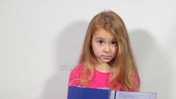 La chica sorprendida se esconde detrás del libro. Grandes ojos de linda joven con un libro. Chica oculta la cara con un libro — Vídeos de Stock