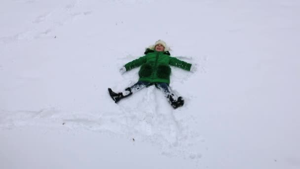 Chica haciendo un ángel de nieve. Muchacha muestra ángel de nieve. Angel de la nieve - niña jugando en la nieve — Vídeos de Stock