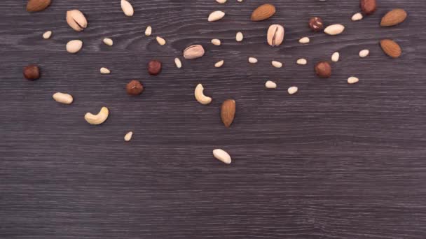 Слово веган, сделанное из разных орехов. Орехи падают и образуют слово веган на темном деревянном фоне. Стоп-движение — стоковое видео