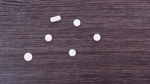 Білі таблетки і капсули розкидані на темному дерев'яному тлі. Чорний напис на білих ліках. Зупинити рух — стокове відео