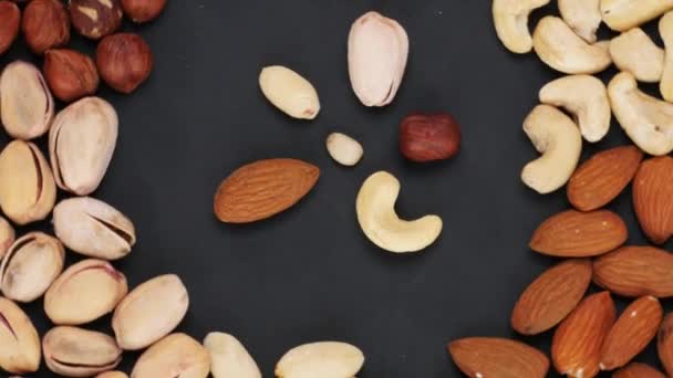 Flor hecha de nueces rodeada por una variedad de nueces en el fondo oscuro. Pétalos giratorios de flores hechos de nueces . — Vídeo de stock