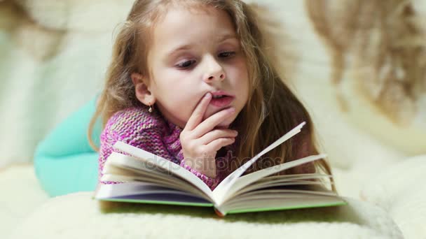 A menina lê entusiasticamente o livro em uma atmosfera acolhedora . — Vídeo de Stock