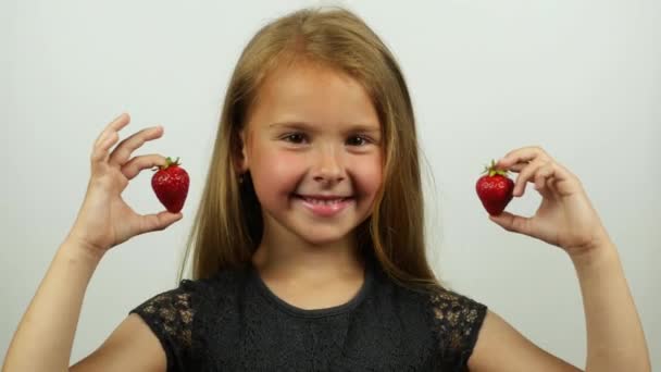 Gros plan de jolie fille tenant des fraises comme boucles d'oreilles. Souriant belle fille avec de délicieuses fraises. Une fille essayant des bijoux de fraises . — Video