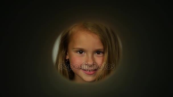 A view through a round hole on the smiling girl. The girl looks from different sides through the peephole. — Stock Video