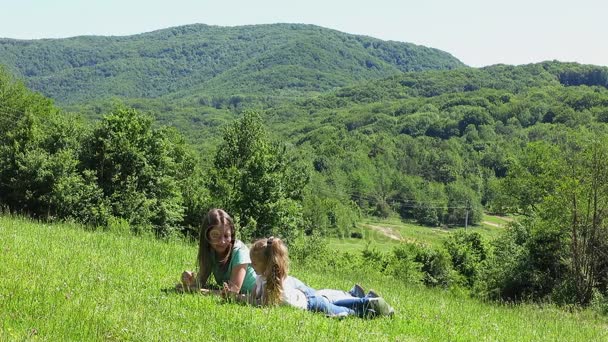 Mutter und Tochter liegen im Gras vor dem Hintergrund hoher Berge. — Stockvideo