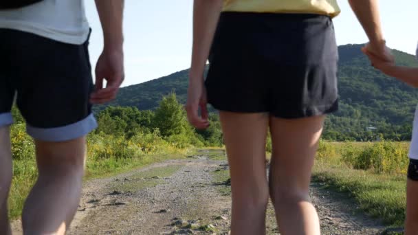 Man, woman and child go by a straight mountain road. Back view of family walking on the trail. Young family with little girl goes hiking. — Stock Video